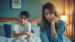 © Santy Hong - Unhappy - stressful Asian woman sitting and crying on the bed while her husband sleeping, a family and post marriage problem. Arguing Asian young couple with bad - negative relationship.