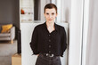 © contrastwerkstatt - Serious Young Woman in Black Blouse Leaning Against Cabinet in Office
