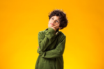 Thoughtful child boy holds chin on yellow background. Dreaming concept