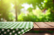 Empty wooden table with green and white checkered tablecloth in front of blurry background with blurry garden background