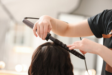 hair styling. hairdresser curling woman's hair in salon, closeup