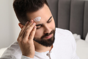 Poster - Man with dry skin applying cream onto his forehead indoors