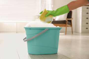 Sticker - Woman holding sponge with foam over bucket indoors, closeup. Cleaning supplies