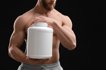 Canvas Print - Young man with muscular body holding jar of protein powder on black background, closeup. Space for text