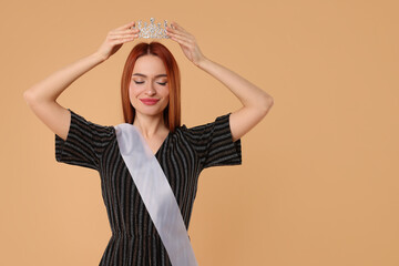 Poster - Beautiful young woman with tiara and ribbon in dress on beige background, space for text. Beauty contest