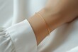 Thin gold bracelet on a woman's hand in a white blouse. Quiet luxury concept.