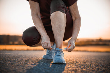 Woman tying shoelace on her running shoes. Getting ready to run. Preparation before jogging on road during sunset. Fitness and sport activity