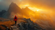 A solitary hiker in a red jacket ascends a rocky mountain path against a stunning backdrop of golden sunrise and misty mountain peaks