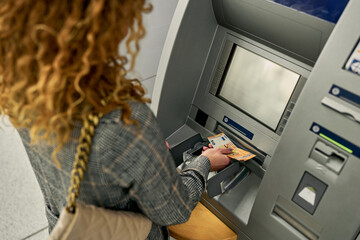 Zooming in on the moment, the woman confidently retrieves crisp bills from the ATM, completing a seamless and secure financial transaction.