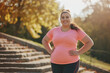 © wolfhound911 - Happy young overweight woman having active fitness workout outside. Fat chubby plump lady in sports clothes standing on stone staircase in beautiful city park, doing lateral bend exercise and smiling