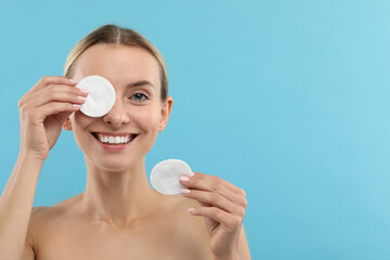 Poster - Smiling woman removing makeup with cotton pads on light blue background. Space for text