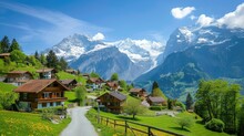 Idyllic Swiss Village With Wooden Chalets, Green Fields, And Snow-capped Mountains Under A Clear Blue Sky.