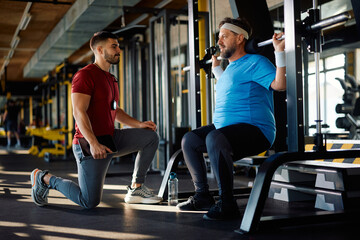 Wall Mural - Middle aged athlete having weight training with coach while working out in gym.