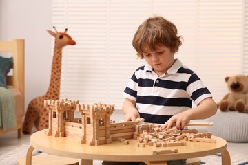 Poster - Cute little boy playing with wooden construction set at table in room. Child's toy