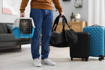 Sticker - Travel with pet. Man holding carrier with cute cat and bag at home, closeup