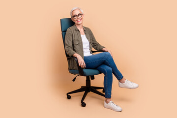 Sticker - Full length photo of lovely pensioner lady sitting armchair office manager wear trendy khaki garment isolated on beige color background