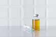 Glass bottle of injectable medicine and a syringe on white medical or pharmaceutical laboratory table. Textured white background.