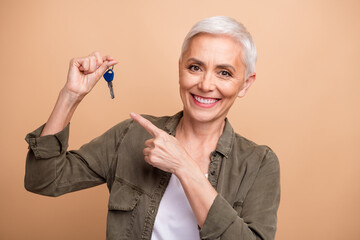 Sticker - Portrait of happy mature lady in shirt direct finger demonstrate she bought new keys her sports car isolated on beige color background