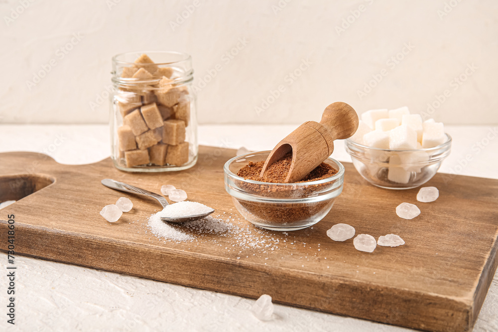 Wooden board with different types of sugar on white background