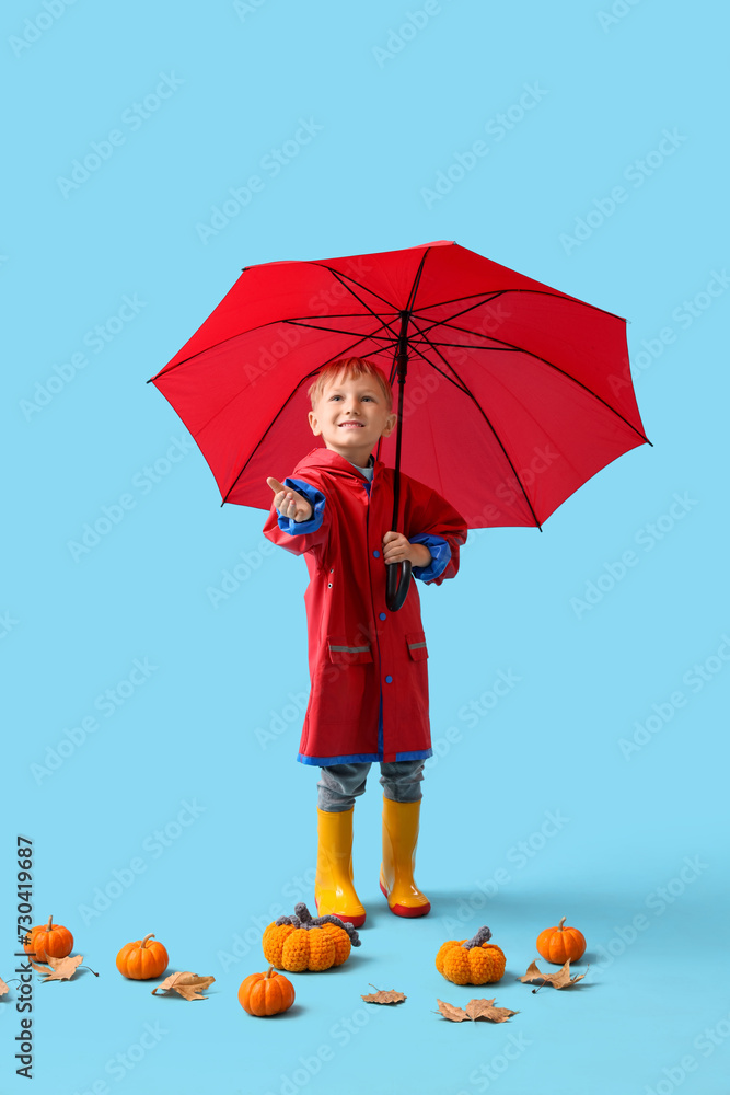 Little boy in rubber boots with umbrella and pumpkins on blue background
