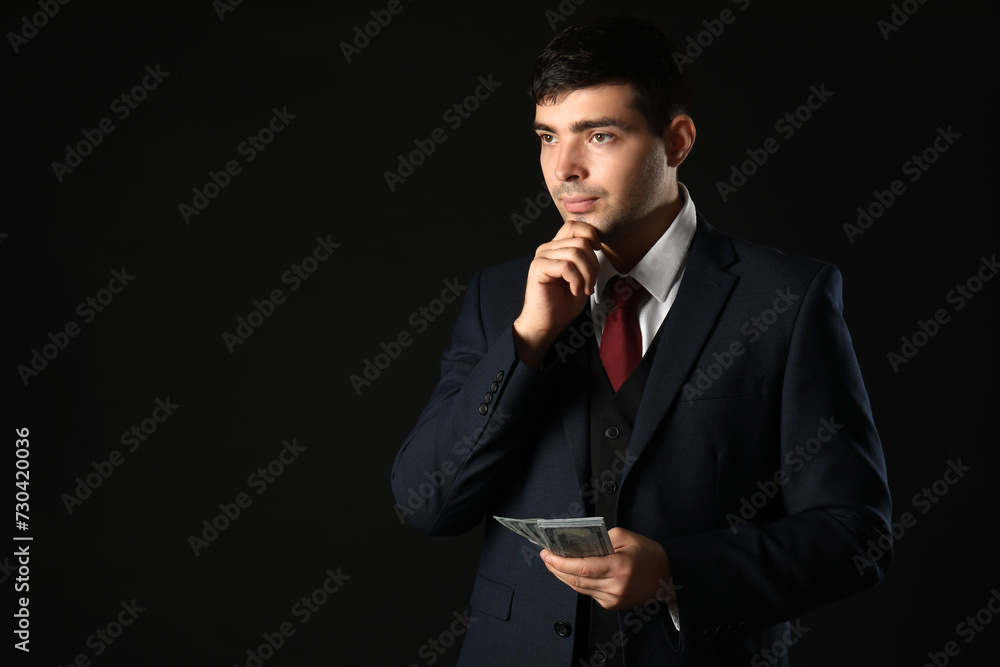 Thoughtful young businessman with bribe on dark background