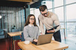 © DSMT - Colleagues communicate while working with a laptop in the office. Two workers in a modern workspace. Two young businessmen are sitting together at a table.