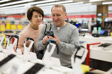 Wall Mural - European man who came to an electronics store with his wife chooses a mobile phone to buy it