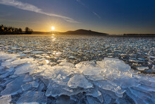Beautiful sunset over the Pálava Hills. In the foreground, white ice floe lying on the shore of the lake.