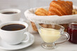 © New Africa - Breakfast time. Fresh croissants, coffee, sweetened condensed milk and jam on white table, closeup