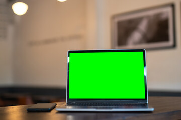 Wall Mural - Mockup of laptop computer with empty screen ,ice coffee and smartphone on table side the window in the coffee shop at the cafe,Green screen