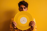 Fototapeta  - Young  man wearing costume holding old vinyl retro record. Vinyl gramophone record on yellow background. 80s and 90s style. Disco party. Love music concept