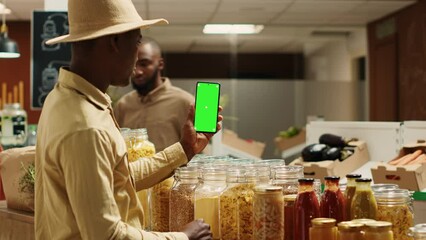 Business owner presenting blank greenscreen display on phone, showing isolated mockup layout in zero waste eco store. African american vendor using chromakey template on mobile phone. Camera A.