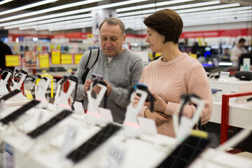 Wall Mural - European man who came to an electronics store with his wife chooses a mobile phone to buy it