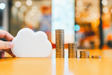 A Pile Of Money Arranged From Low To High With A Hand Holding A Wooden Cloud Model, It Is A Concept Of Cryptocurrency That Is Deposited In The Cloud.