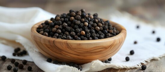 Poster - Numerous black peppercorns rested in a wooden bowl on a white cloth.