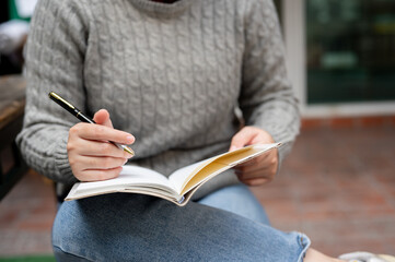 A woman keeping her diary or writing something in her notebook while sitting outdoors.