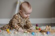 baby in animalprint onesie playing with wooden toys