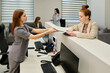 © pressmaster - Side view of young female clinician helping client looking through medical document while standing by administrator counter