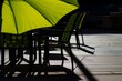 bright umbrella casting shadow on empty chairs and table