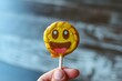 closeup of a hand holding a lollipop with an emoji face on it