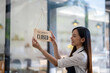© Wasana - Asian female entrepreneur turning the 'Sorry We Are Closed' sign with a content smile after a day's work at her cafe..