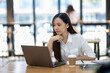 © Wasana - A thoughtful young professional woman concentrates while working on her laptop in a modern office setting..