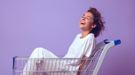 Wall Mural - A happy emotional young woman wearing a white T-shirt and trousers sits in a shopping cart on a bright purple background with a copy space. Discounts, sale, bargain shopping concepts.