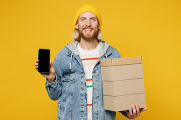 Canvas Print - Young man wear denim shirt hoody beanie hat casual clothes hold stack cardboard blank boxes use blank screen mobile cell phone isolated on plain yellow background studio portrait. Lifestyle concept