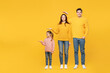 © ViDi Studio - Full body young fun happy parents mom dad with child kid girl 7-8 years old wear pink sweater casual clothes hold hand above head show height isolated on plain yellow background. Family day concept.
