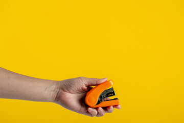 Wall Mural - Orange stapler in hand isolated on yellow background
