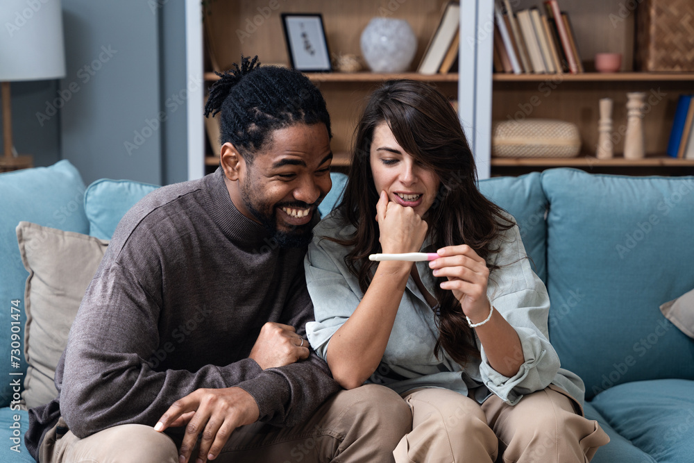 Expectations, wanted or unwanted pregnancy. Young couple man and woman sitting at home on sofa holding and looking at pregnancy test. New life concept, waiting for positive or negative pregnant result