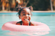 African American joyful laughing girl in the pool, floating on a pink swimming ring on a sunny day.