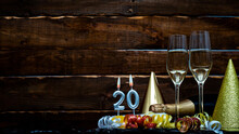 Solemn Background For The Anniversary With The Number  20. Happy Birthday Background On Brown Wooden Background With Champagne Bottle And Champagne Glasses. Beautiful Holiday Decorations Copy Space.