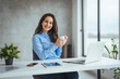 © Dragana Gordic - An attractive young businesswoman having coffee while working at her office desk. Laughing young  female entrepreneur drinking a cup of coffee
